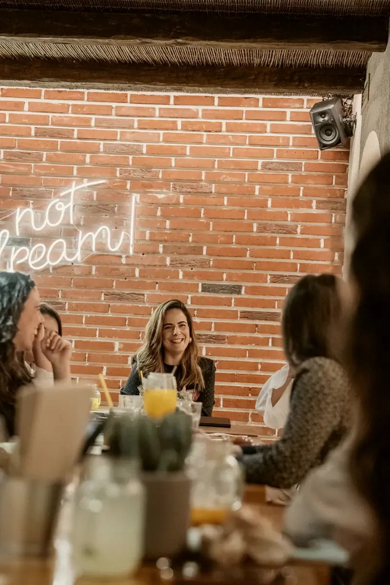 Conversa à mesa vista por entre copos e mulheres desfocadas.